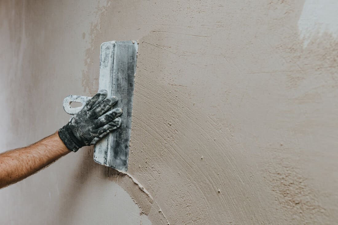 Male builder in work overalls plastering a wall using a construction trowel. 