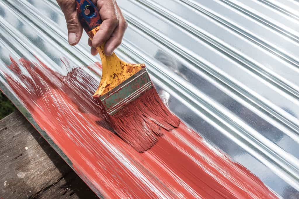 Man painting the roofing with a red colored paint