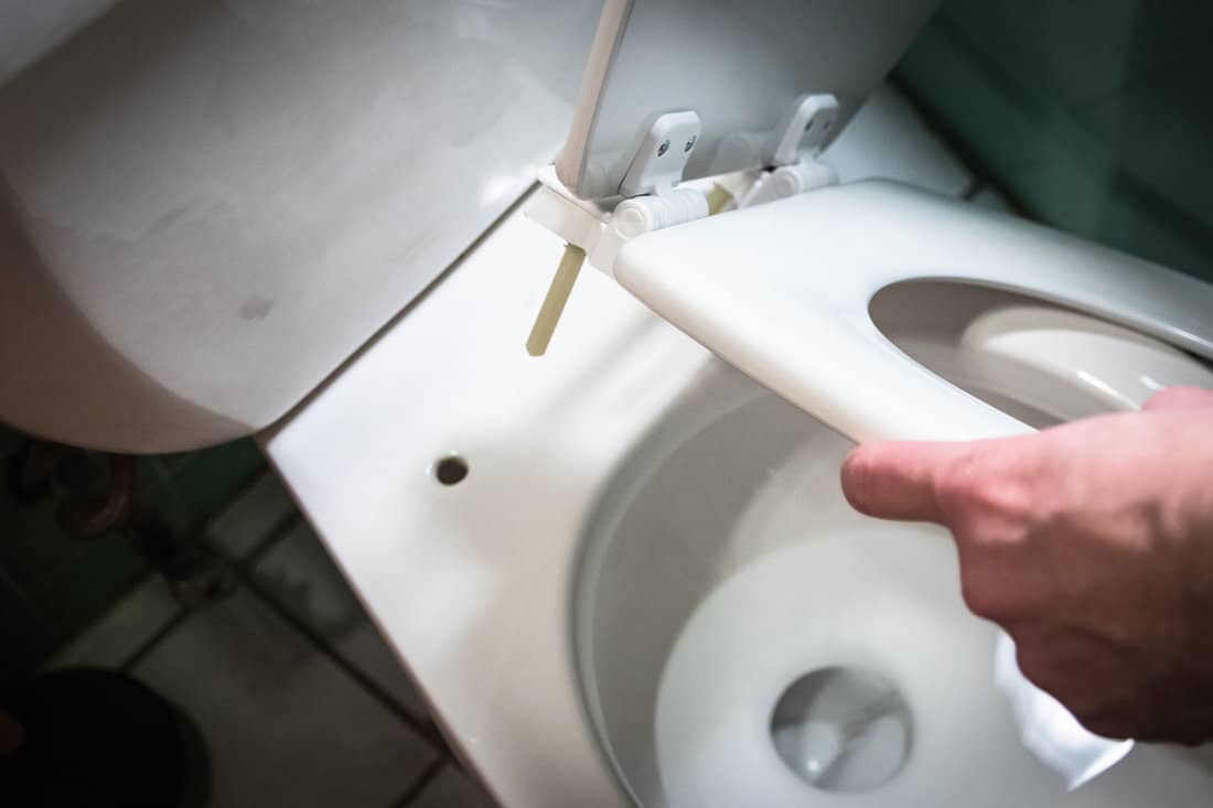 Man's hands installating or removing consumer home toilet seatlid