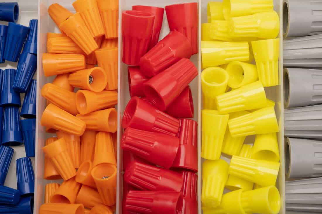 Many colored wire nuts in plastic box on white background , Tool for connecting electrical wires