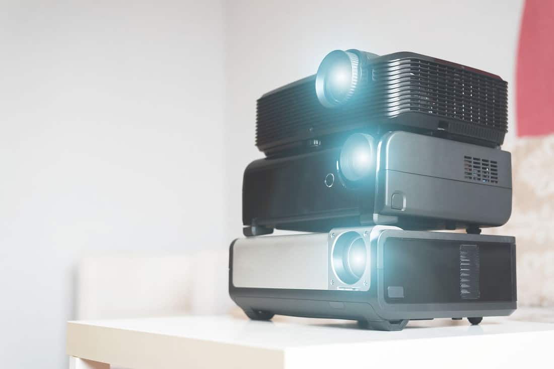 Many stacked projectors on a table on a sofa background. 