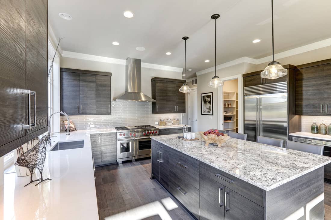 Modern gray kitchen features dark gray flat front cabinets paired with white quartz countertops and a glossy gray linear tile backsplash. 