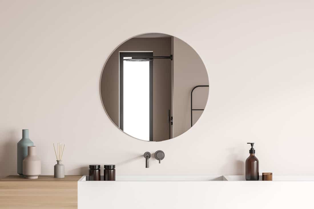 Modern vanity design, using wood-look material pairing with white ceramic sinks and a stylish round mirror on the beige wall of the shower room.