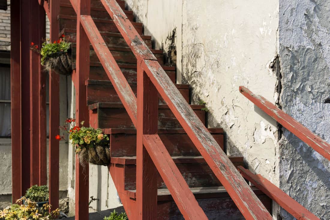 Old, exterior wooden staircase with red, peeling paint and cracked