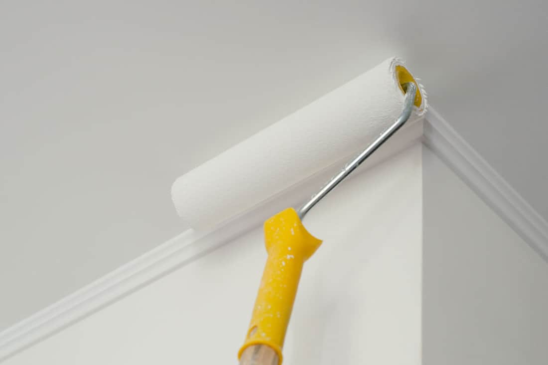 Paint roller with yellow handle. Ceiling and wall painting process