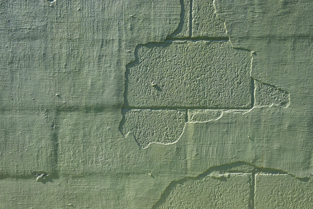 Peeling green paint plaster over concrete cinder block wall 