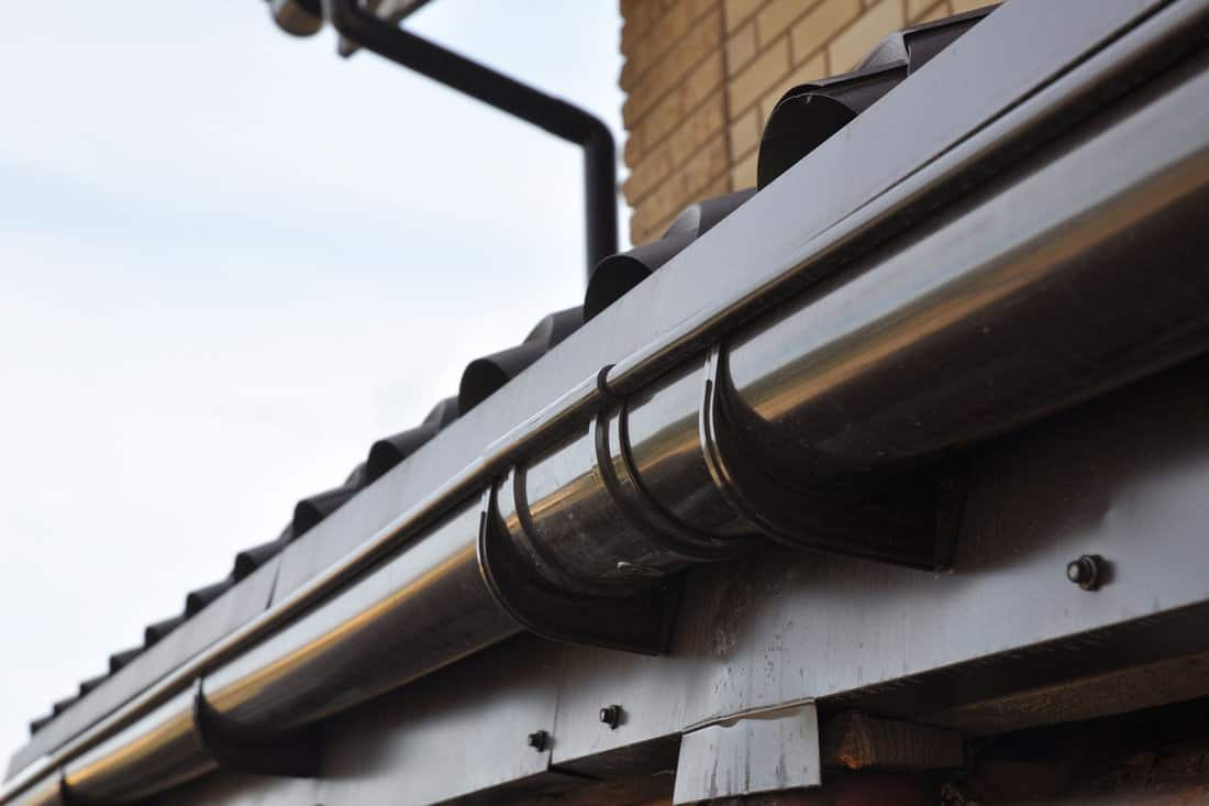 Plastic roof gutter installation with a close-up of a rain gutter joint, joiner, brackets and hangers. Roof gutter repair to prevent water leaks near a joint. 