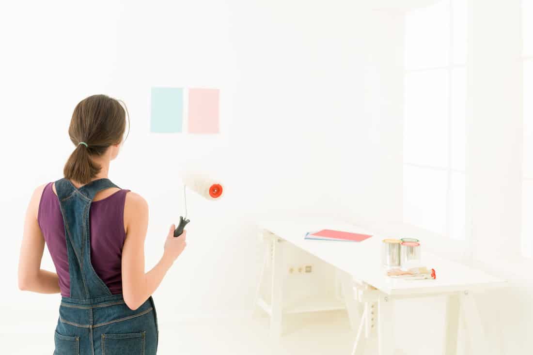 Rear view of a woman holding a paint roll choosing colour for painting a room against white background 
