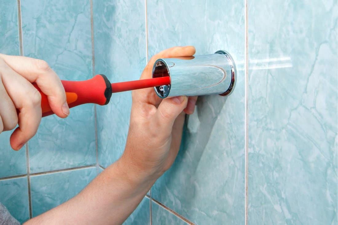 Person fixing the wall holder bracket for a shower using a screwdriver