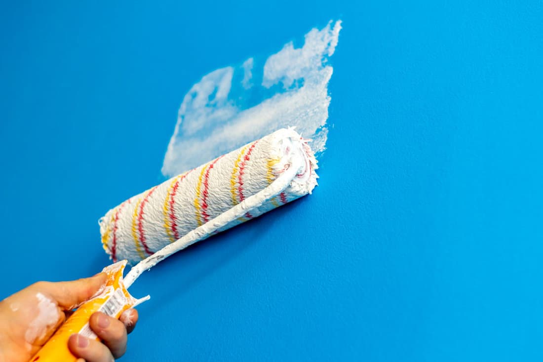 Shot of a hand with a paint roller covered in white paint,painting over a blue wall