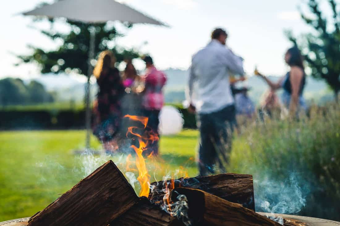 Smokey outdoor fire pit with people gathered together at a party restaurant function in the background