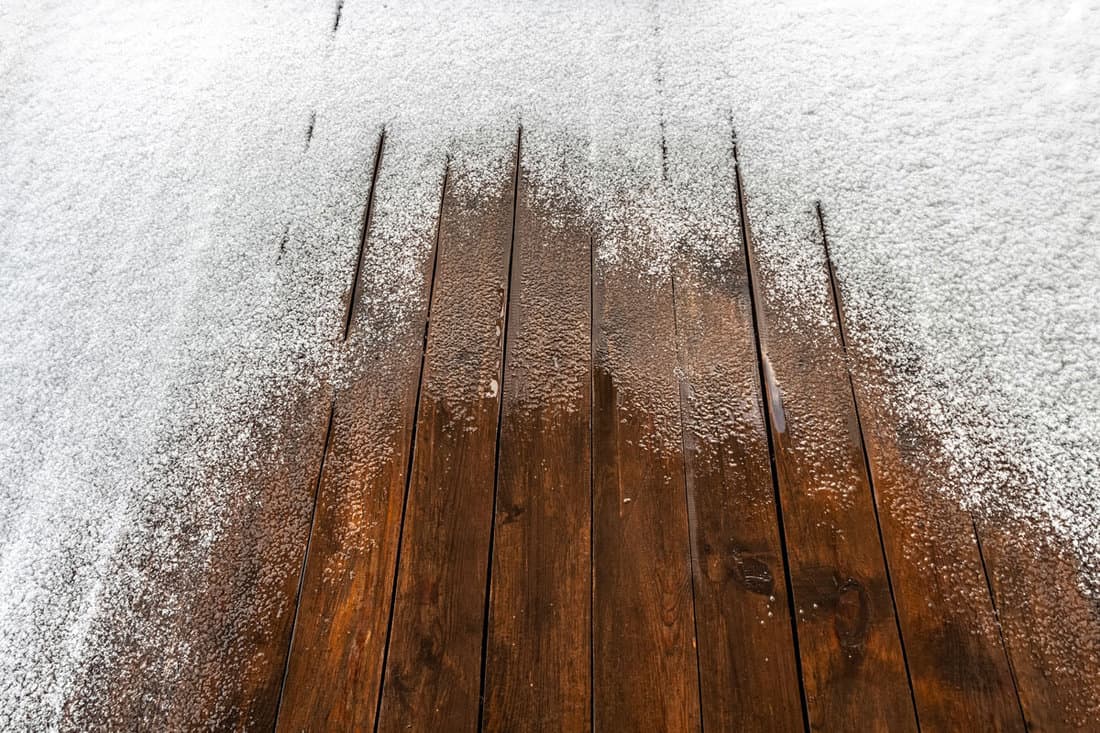 Snow on a wooden plank floor of an open terrace