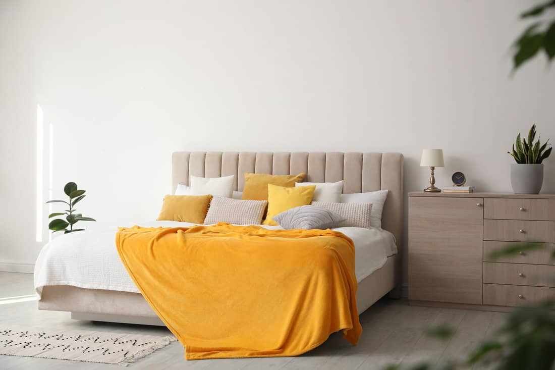 Stylish bedroom interior with soft yellow pillows and blanket