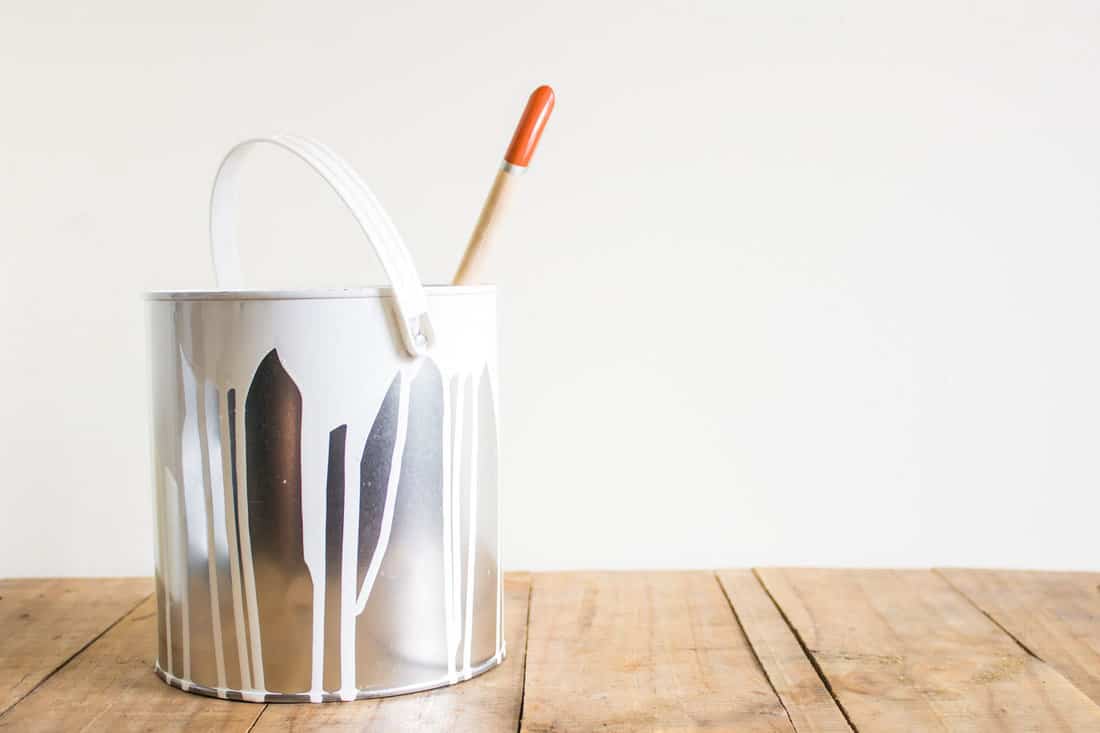 The paint bucket and paint brushes on a wooden table, behind a white background. 