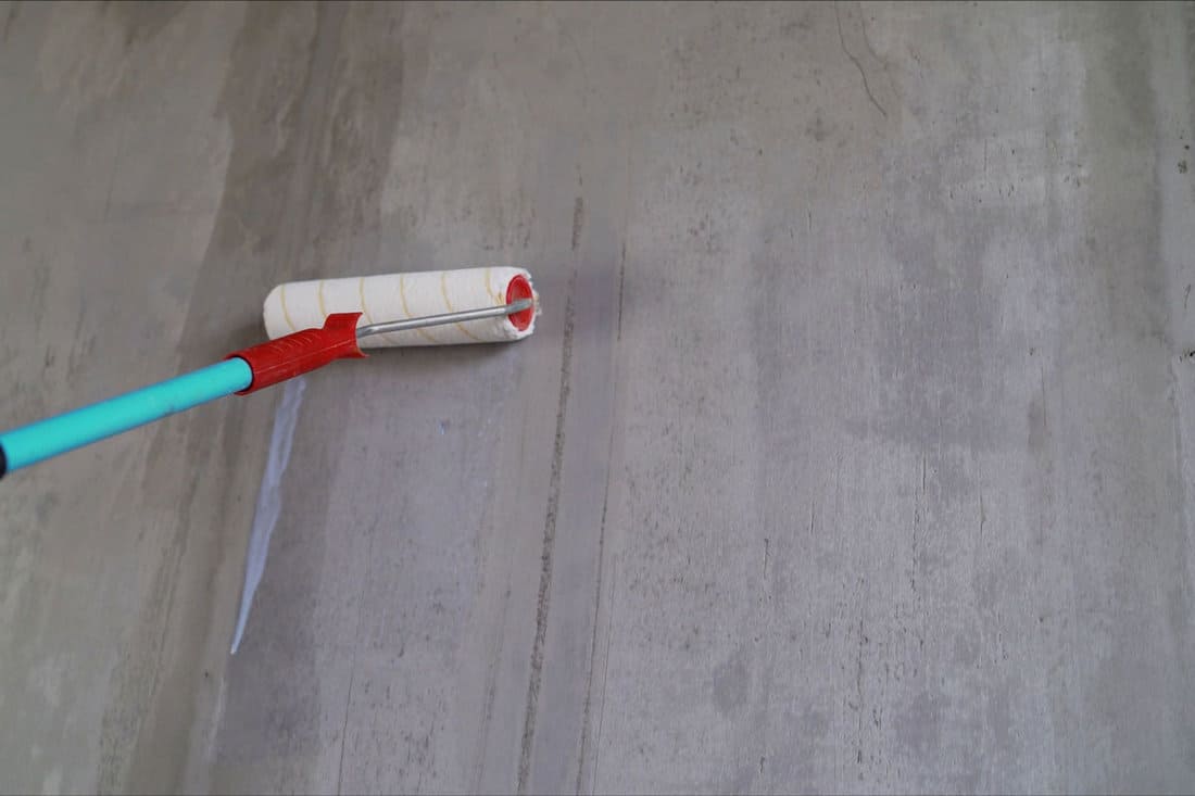 The wall is primed with a roller. A man's hand applies a primer to a concrete wall with a roller