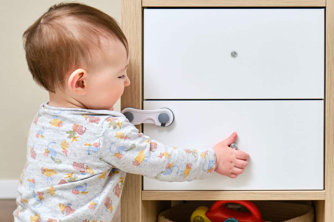 Toddler baby boy rips off a cabinet drawer with his hand. The child holds the cabinet door handle, small kid 