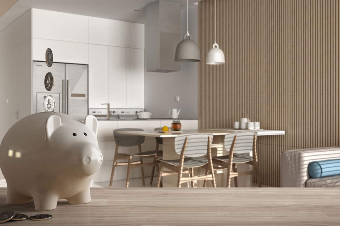 Wooden table top or shelf with white piggy bank with coins, modern white kitchen and dining room, expensive home interior design, renovation restructuring concept architecture, 3d illustration 