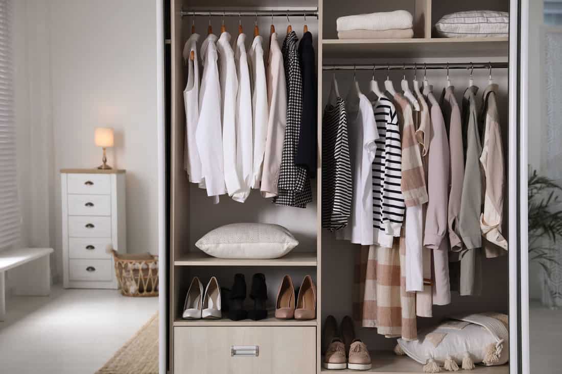 Wardrobe closet with different stylish clothes, shoes and home stuff in room 