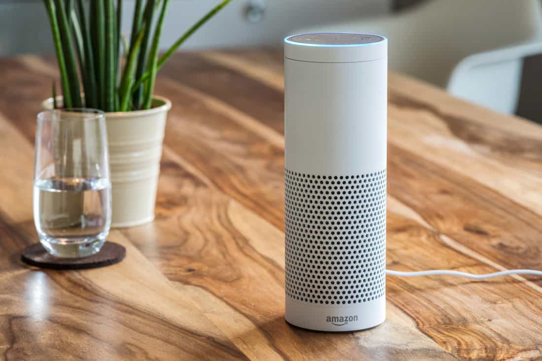 White Amazon Echo Plus, Alexa Voice Service activated recognition system photographed on wooden table in living room, Packshot showing Amazon Logo