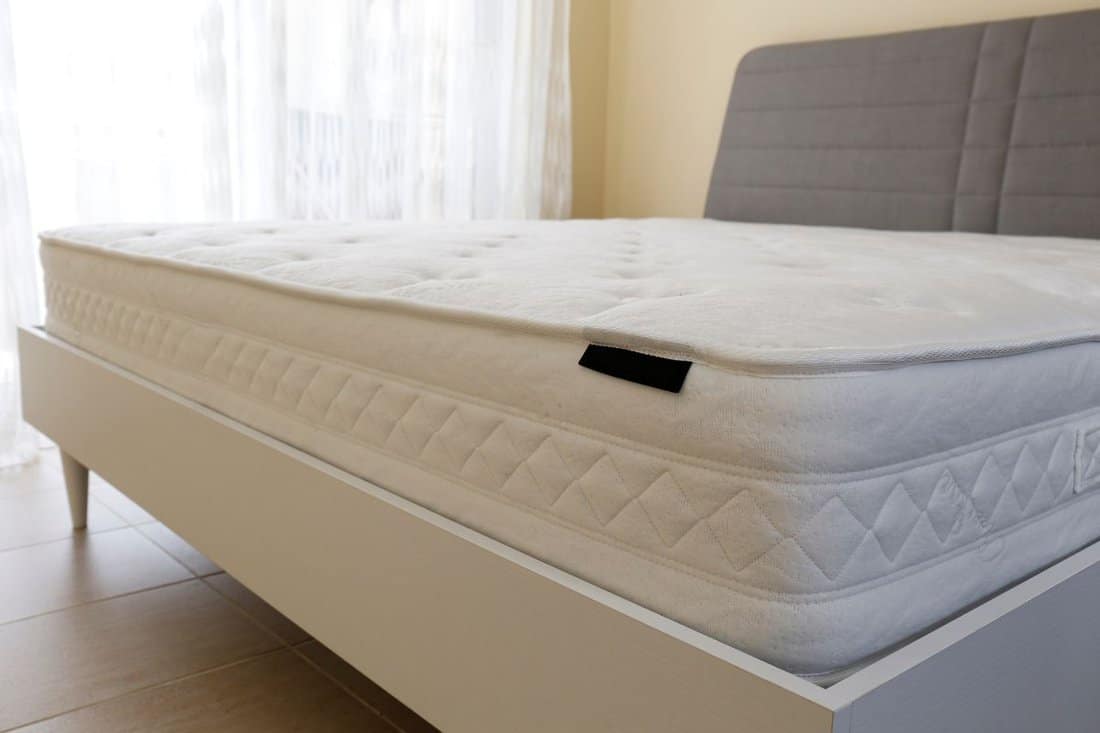 White orthopedic mattress top side surface pattern on unmade bed in the bedroom. Hypoallergenic foam matress for proper spinal alingment and pressure point relief.