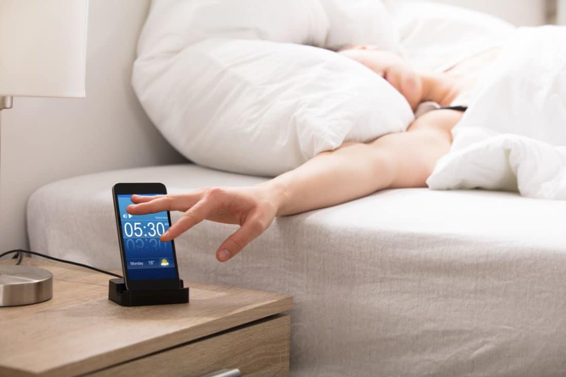 Woman Sleeping On Bed Snoozing Alarm On Smart Phone Screen