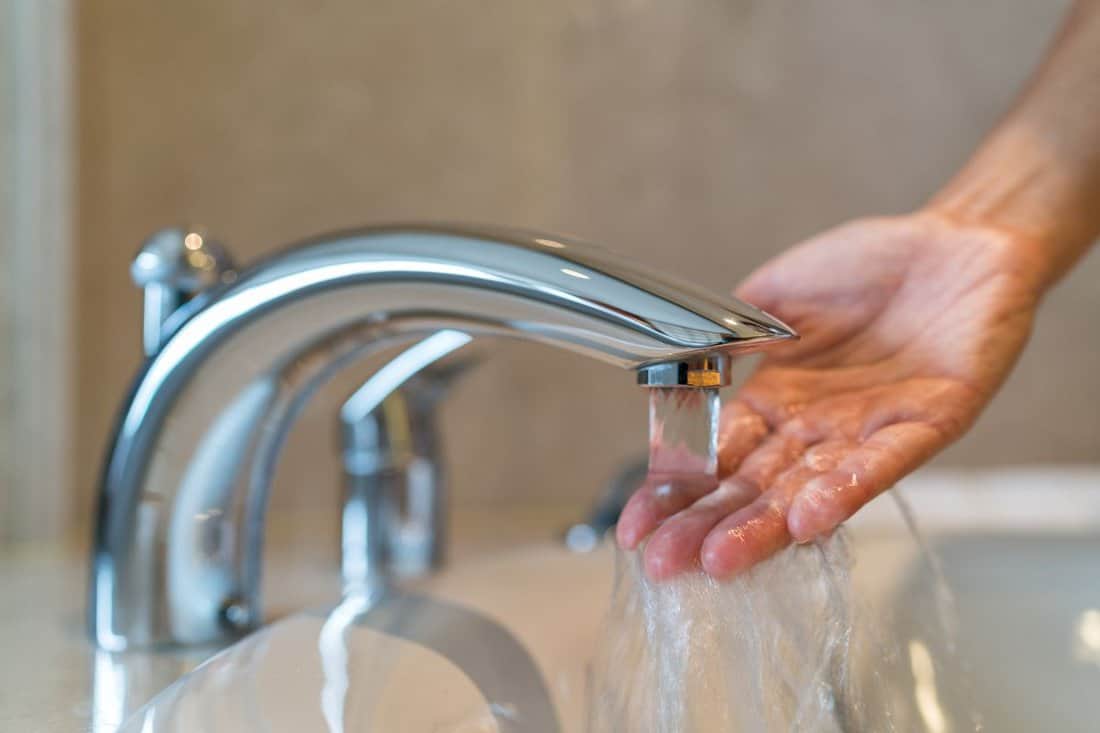 Woman taking a bath at home checking temperature touching running water with hand. 