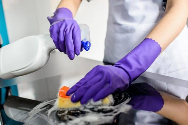 Woman wearing rubber protective gloves and cleaning kitchen countertop, Can You Use Granite Cleaner On Quartz?