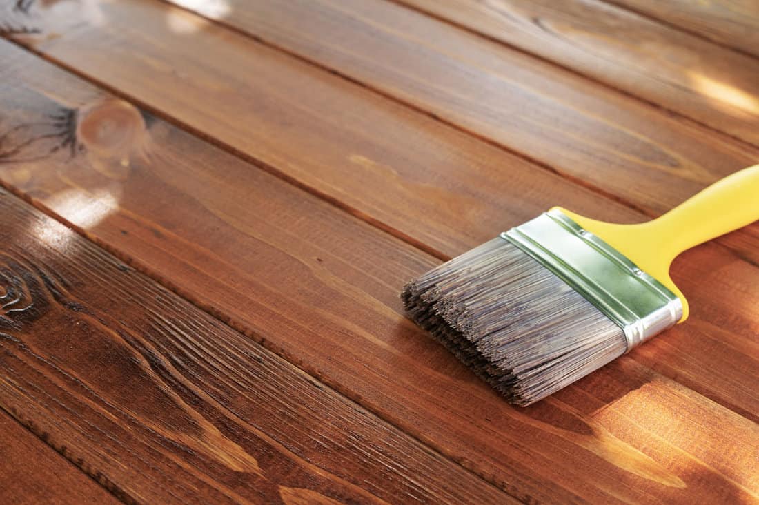 Wood staining diy. Brush. Painting wooden patio deck with protective brown oak varnish. Outdoo