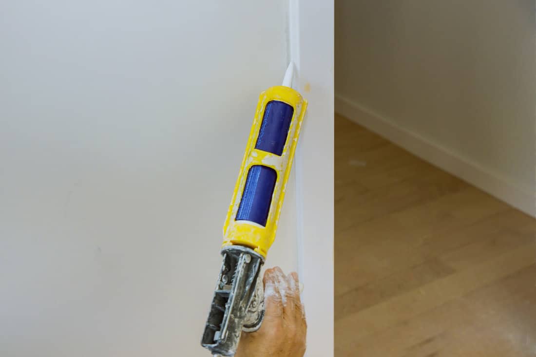 Worker applies silicone sealant spaces tube for repairing of wooden on corner wall door molding trim