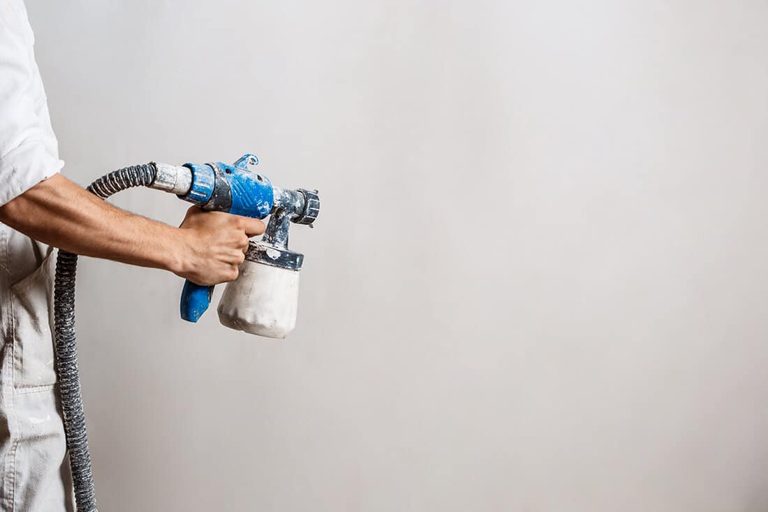 Worker painting wall with spray gun