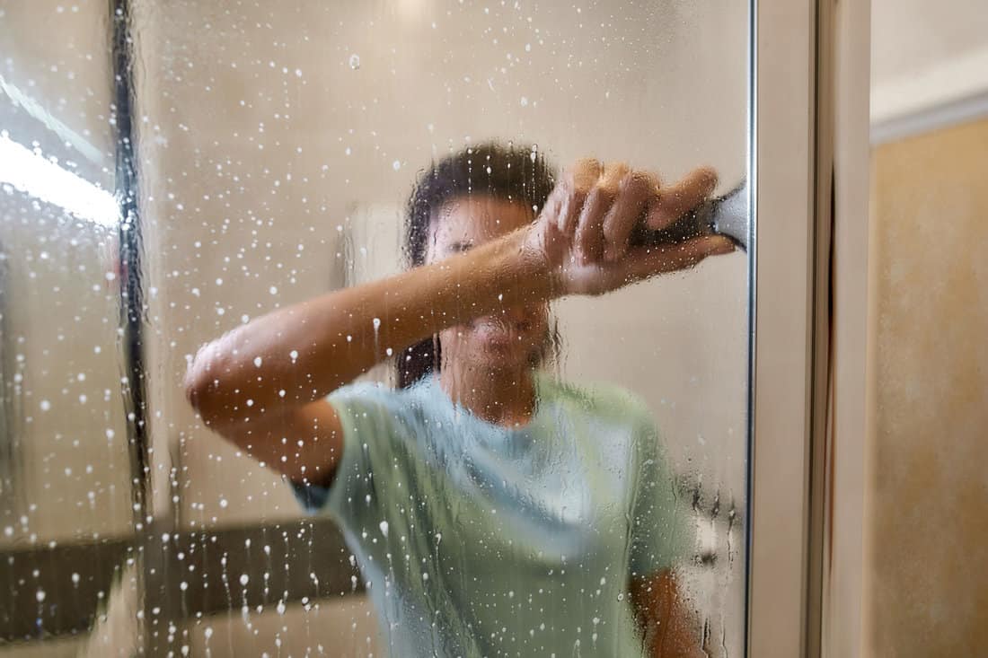 Woman cleaning shower door with squeegee and spray detergent