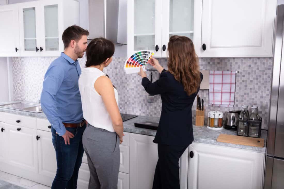 Young Female Real Estate Designer Showing Swatch Palette In New House To Couple