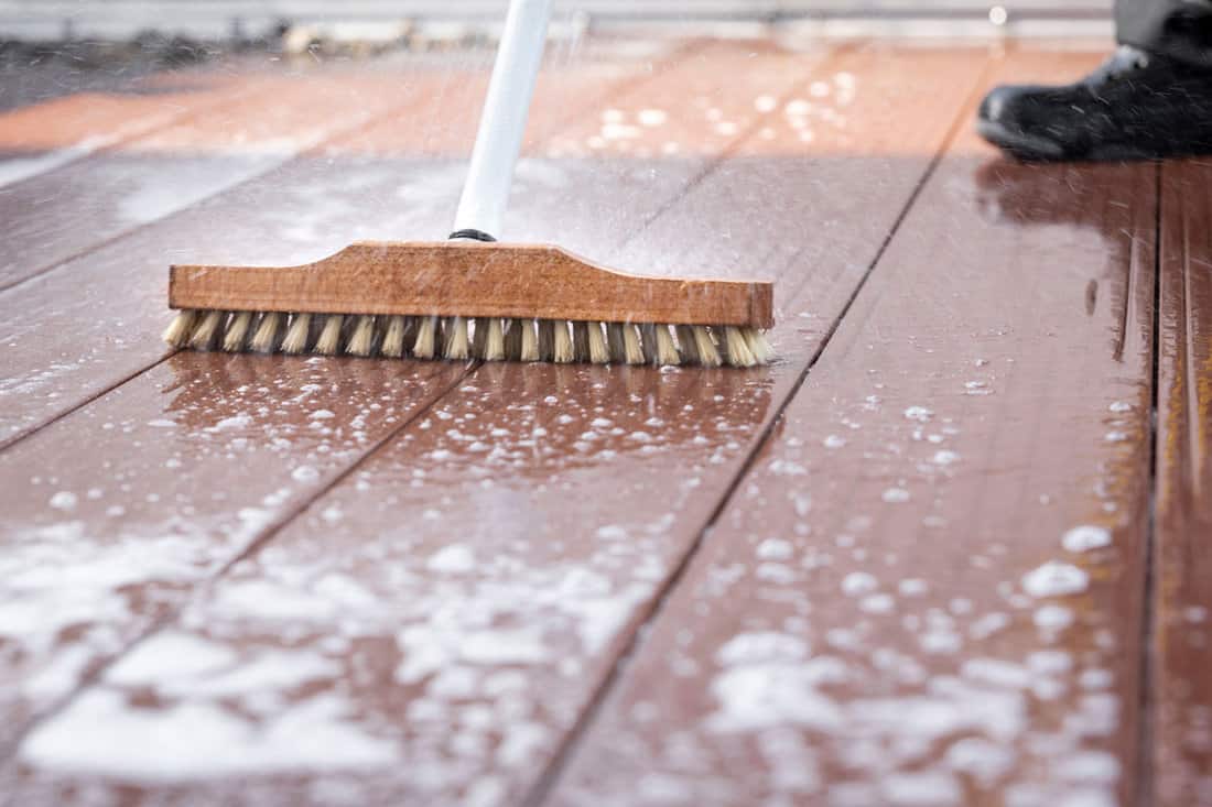 a scrubbing brush during spring cleaning on a wooden terrace with soap and splashes of water