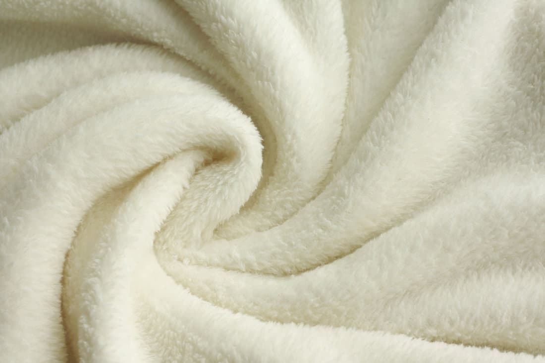a warm, white, plush micro fleece blanket fabric is swirled into a circular pattern background 