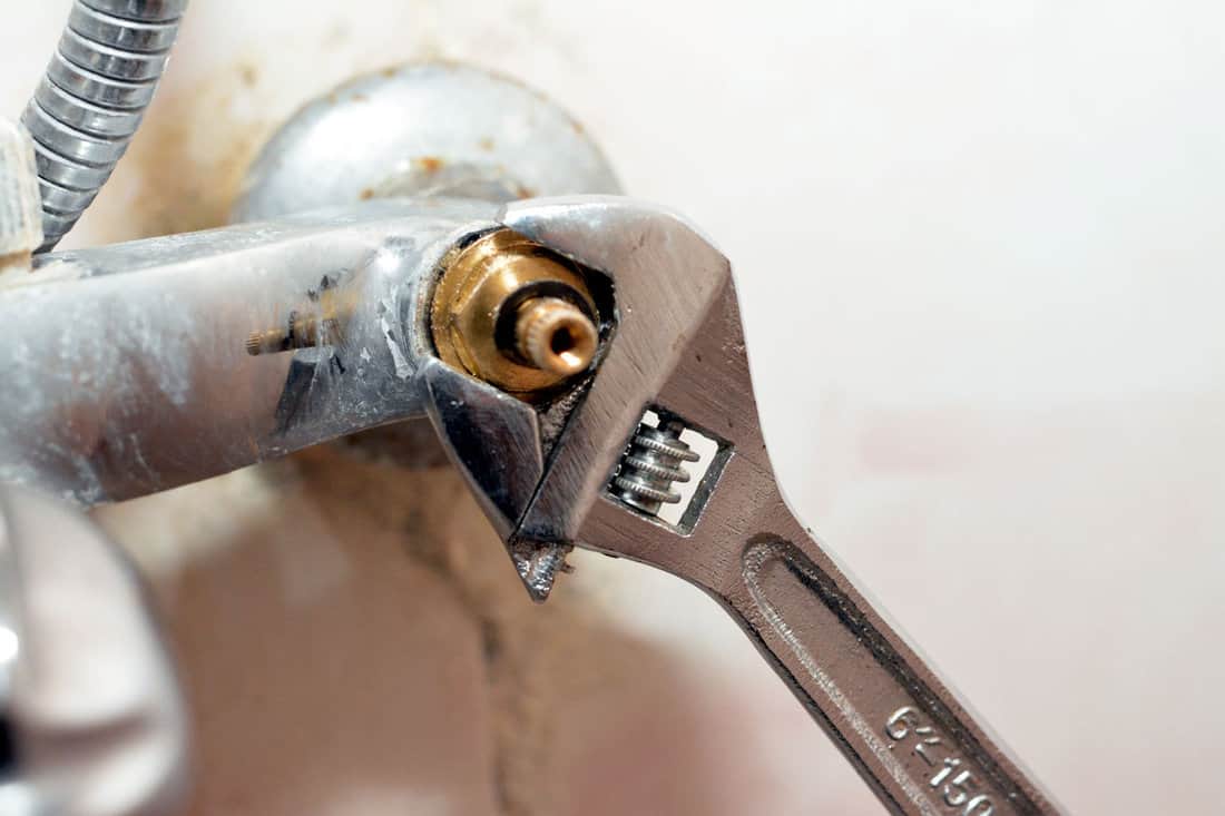 A plumber fixing a problem of a shower faucet tap spinning the cartridge body with an adjustable wrench tool to change it, plumbing and maintenance concept background at home, selective focus 