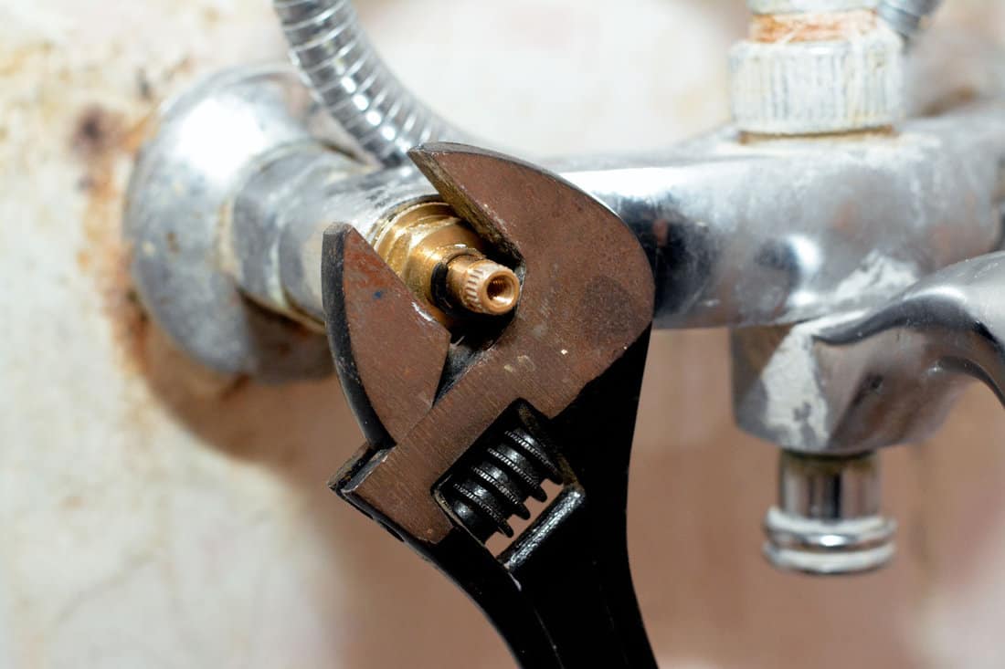 A plumber fixing a problem of a shower faucet tap spinning the cartridge body with an adjustable wrench tool to change it, plumbing and maintenance concept background at home, selective focus 