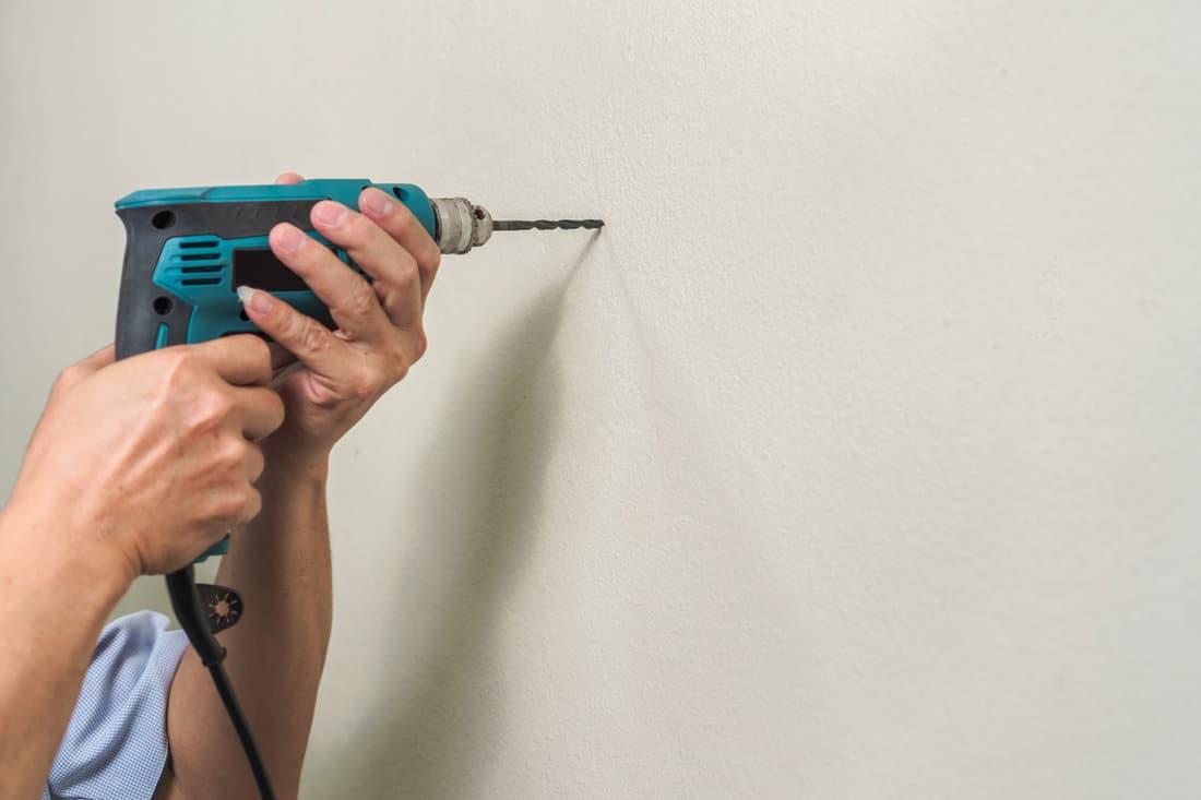 Asian man use electric drill on wall in him house