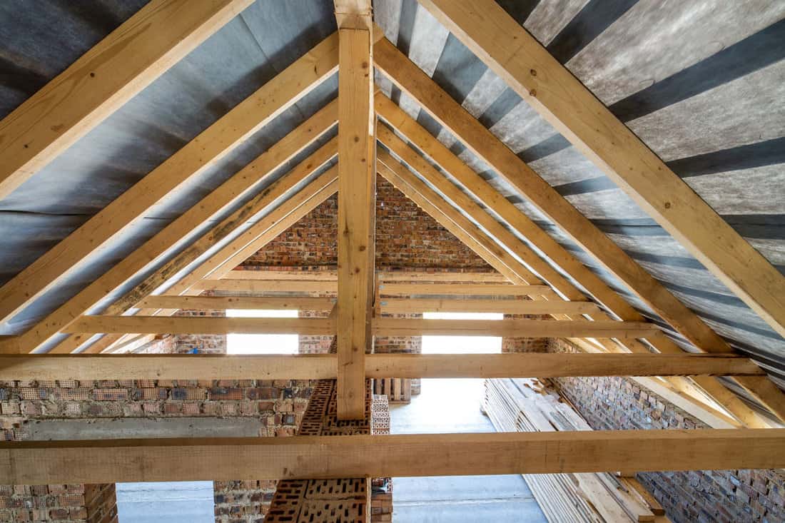 Attic of a building under construction with wooden beams of a roof structure and brick walls. 