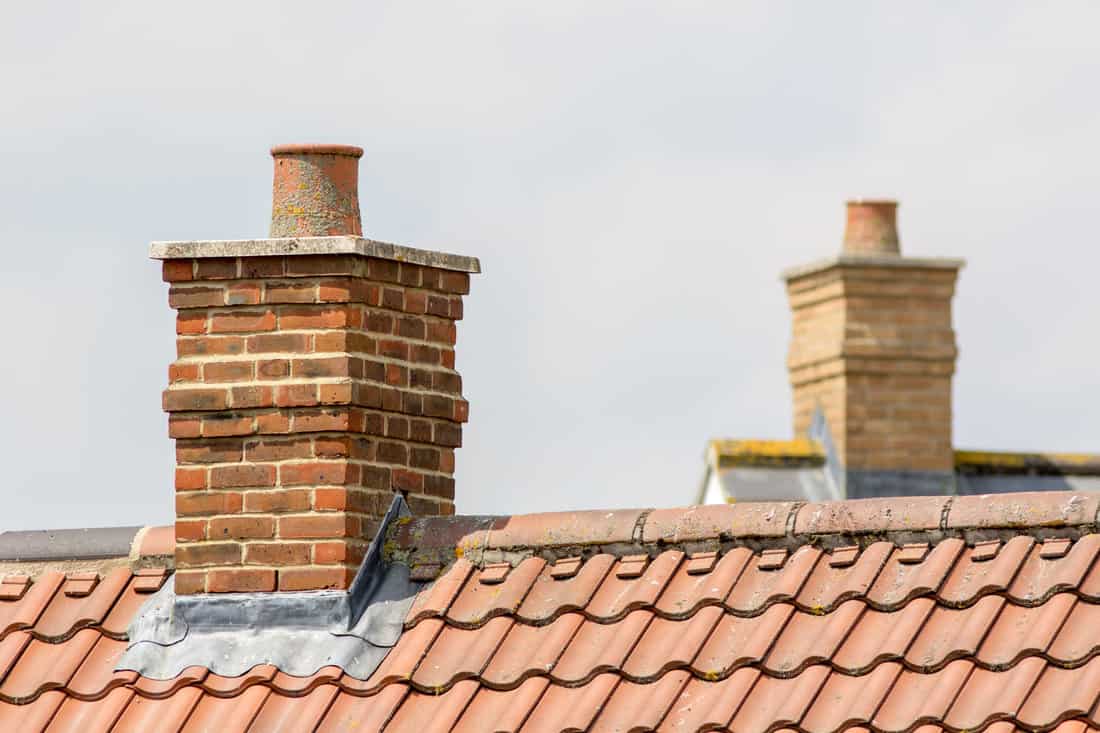Brick chimney stack on modern contemporary house roof top. Urban housing estate tiled roof in close-up. 