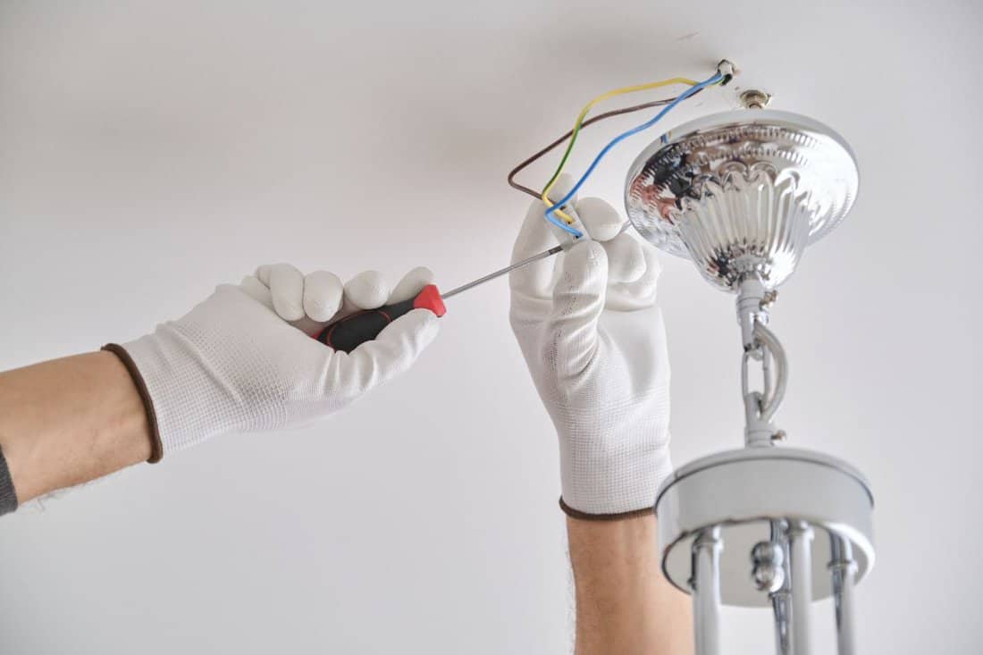 Installation ceiling lamp, hands of male electrician fixing chandelier with use of professional tools.