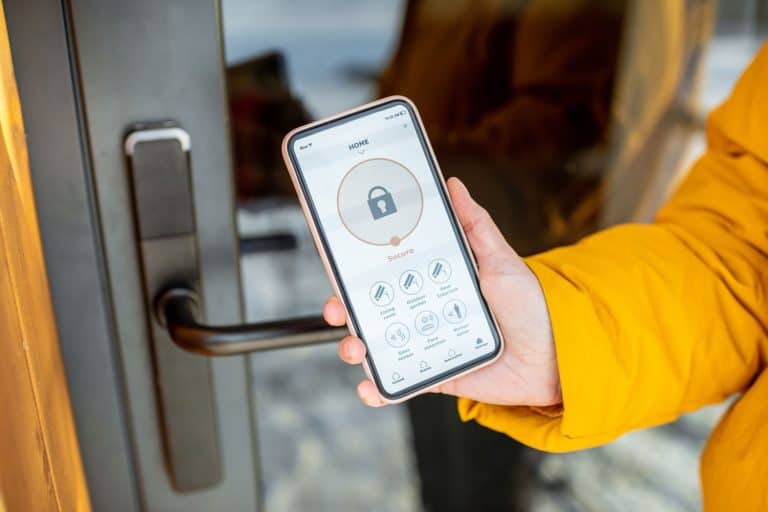 Locking smartlock on the entrance door using a smart phone remotely. Concept of using smart electronic locks with keyless access, Are Kwikset Smart Locks Waterproof [And How Safe Are They]