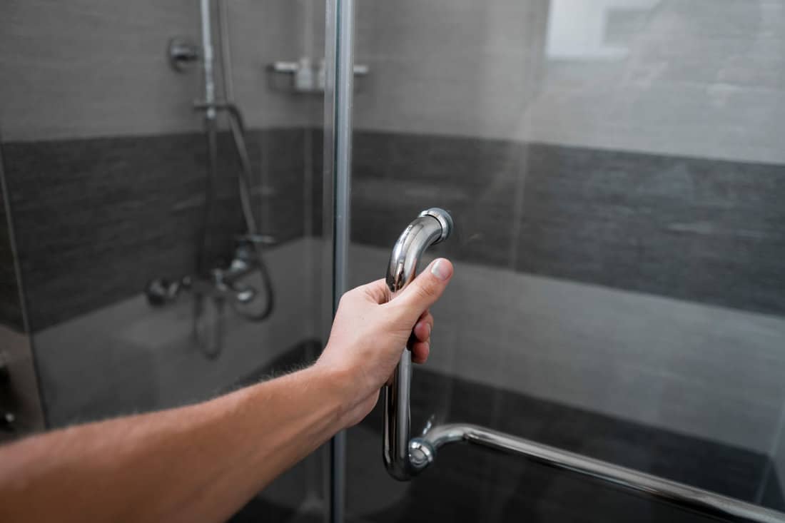 Male hand opens the shower door in a modern bathroom. 