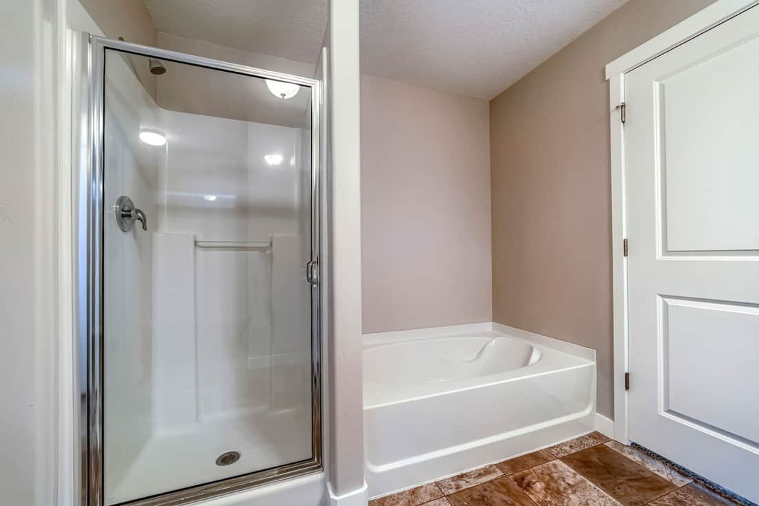 Shower stall and bathtub inside a clean bathroom with brown tiles on the floor 