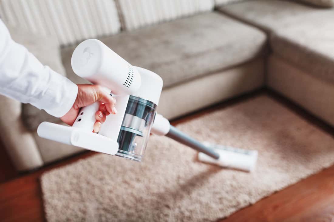 Woman using stick vacumm cleaner to clean the rug