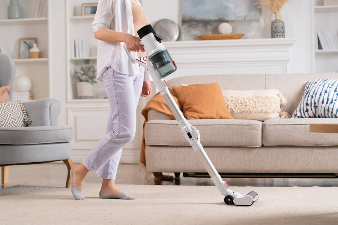 Young woman uses cordless vacuum cleaner to clean home carpet. Modern easy cleaning. 