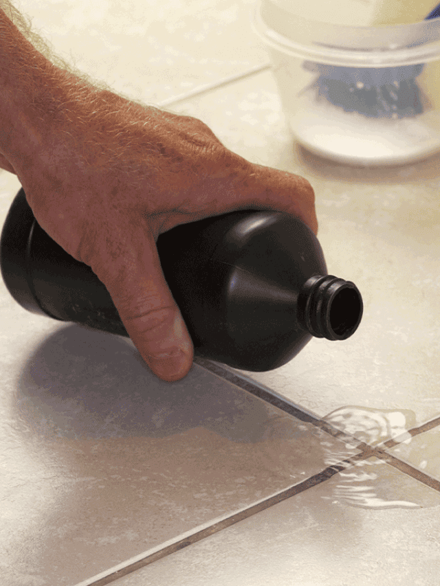 Hand pouring hydrogen peroxide on bathroom floor tile grout