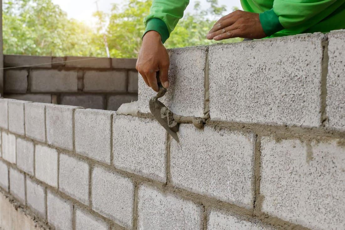 masonry worker make concrete wall by cement block and plaster at construction site.