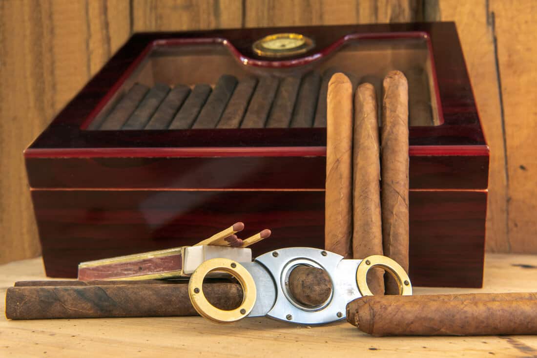A huge box of cigars and other accessories with a cigar cutter and matches
