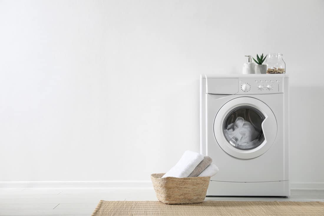 A white washing machine inside a white walled launddry room