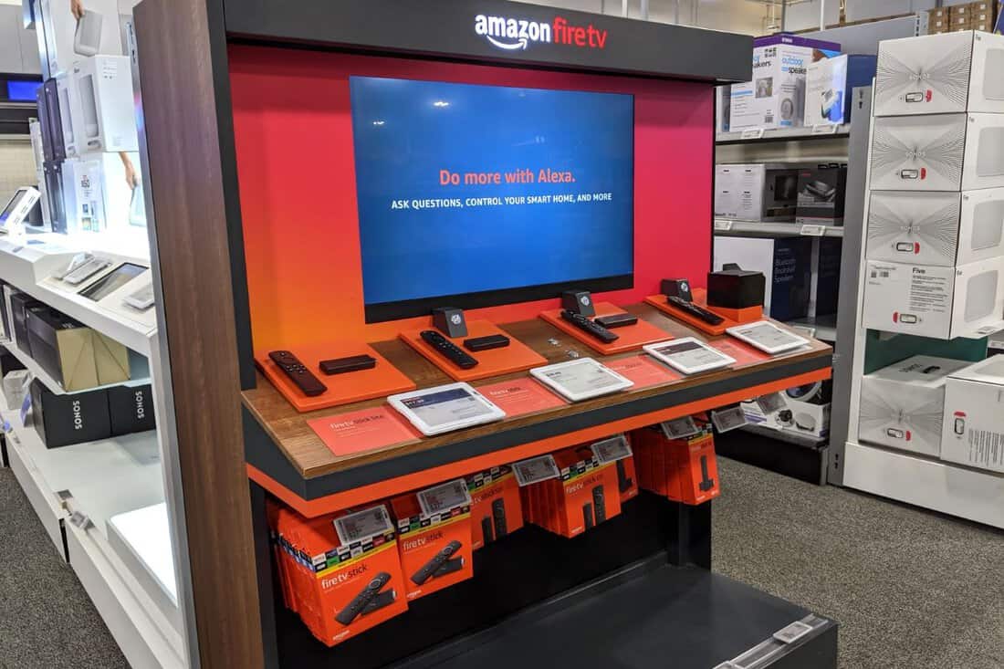 : Amazon Fire TV Display inside Best Buy Store featuring Stick and Cube devices with Alexa. Amazon Fire TV is a digital media player and its microconsole remote.